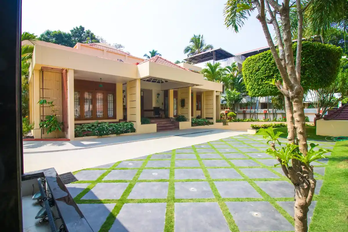 Completed single-storey home seen across its grass-and-paver forecourt, with clipped topiary and lawn, Trivandrum