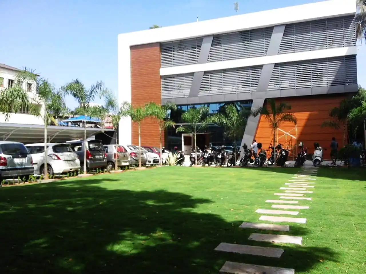 Completed three-storey commercial building in use, seen across its lawn and stepping-stone path, Mangalam, Kerala