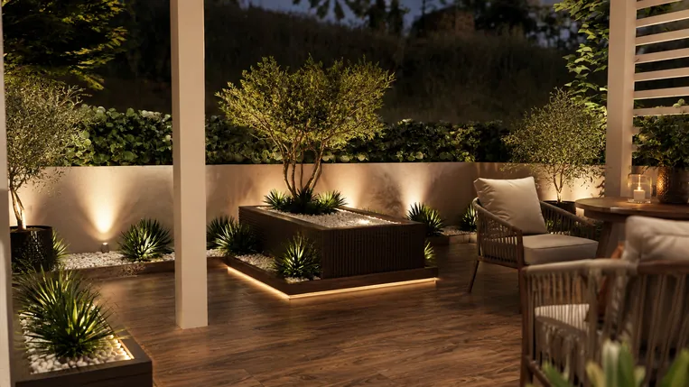Open terrace at night with a timber deck, cane lounge chairs and a lit raised planter with small trees